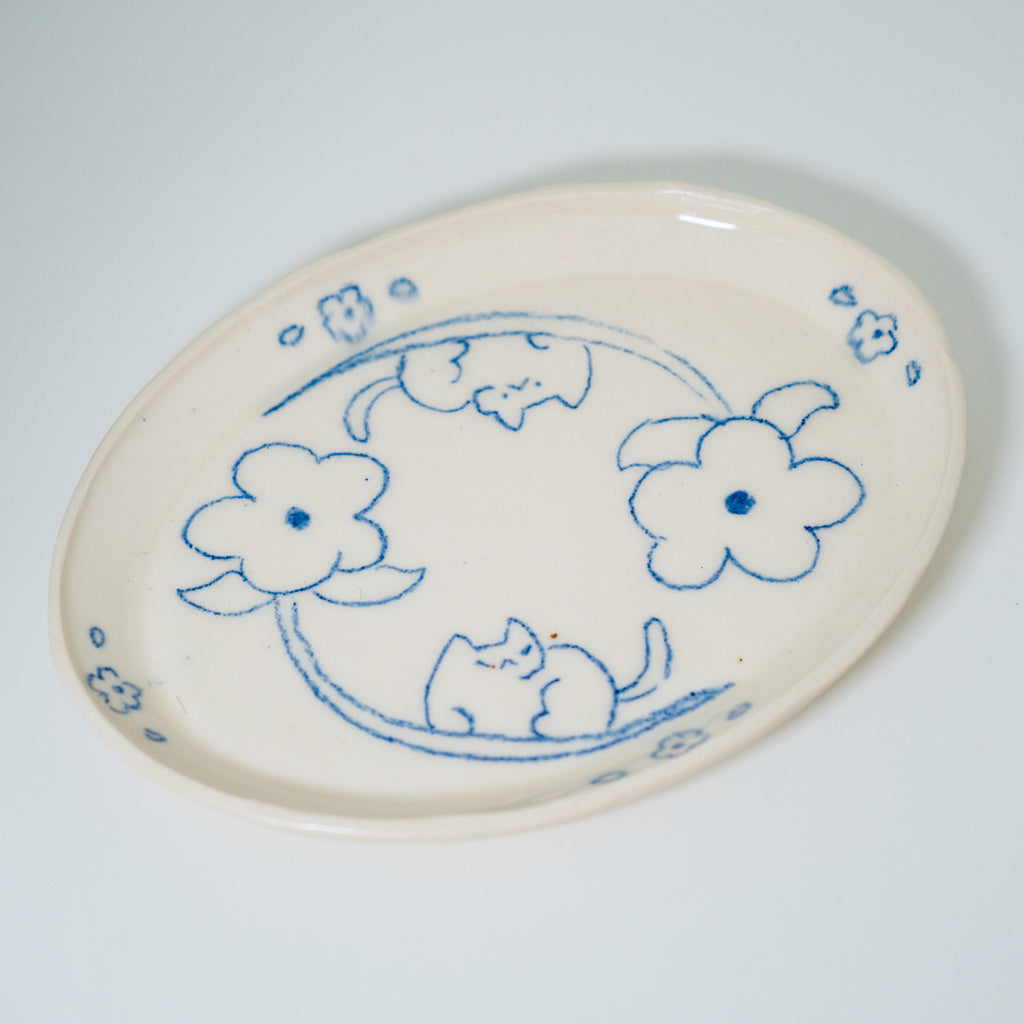 Oval ceramic plate with blue floral and cat design on a white background