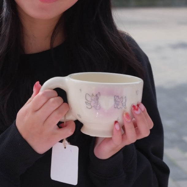 Person holding a ceramic cup outdoors with buildings and trees in the background