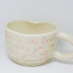 Heart-shaped mug with red text on a white background