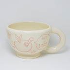 White ceramic mug with red illustrations and text on a white background