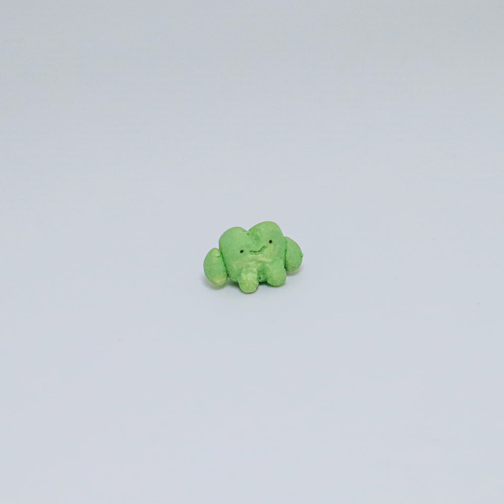 Small green frog ceramic figurine on a light gray background