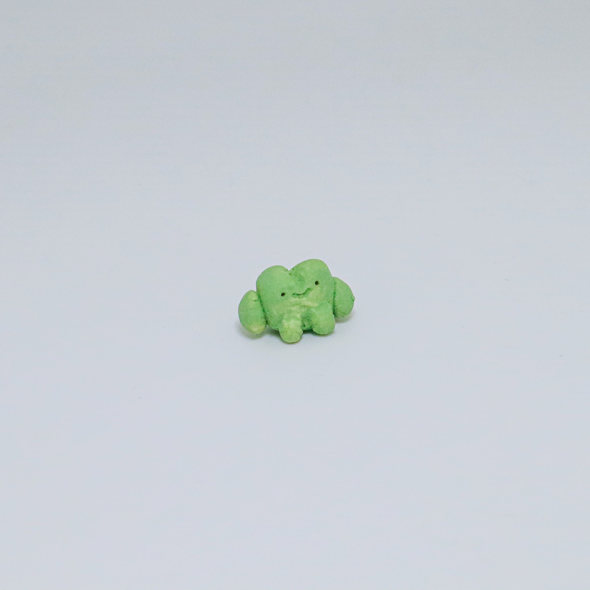 Small green frog ceramic figurine on a light gray background