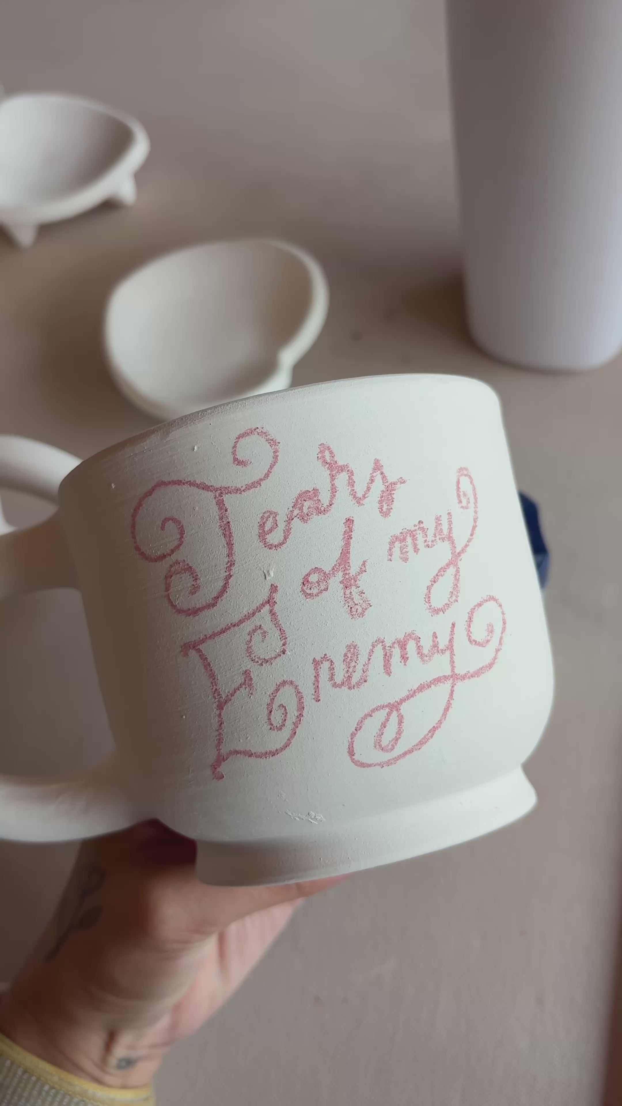 white ceramic mug with red writing on it, with a ceramic studio as the background